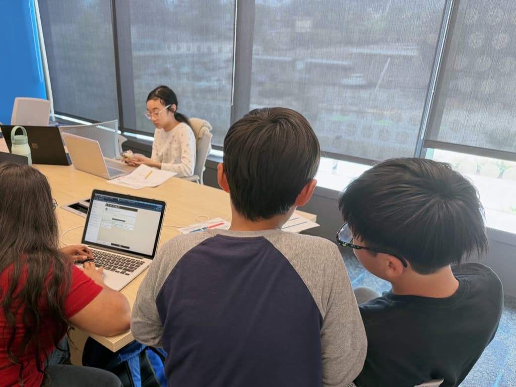 Students building their games on laptops around the table in a small group session