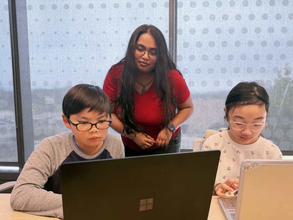 Mentor looking over two students' screens while they work on their games