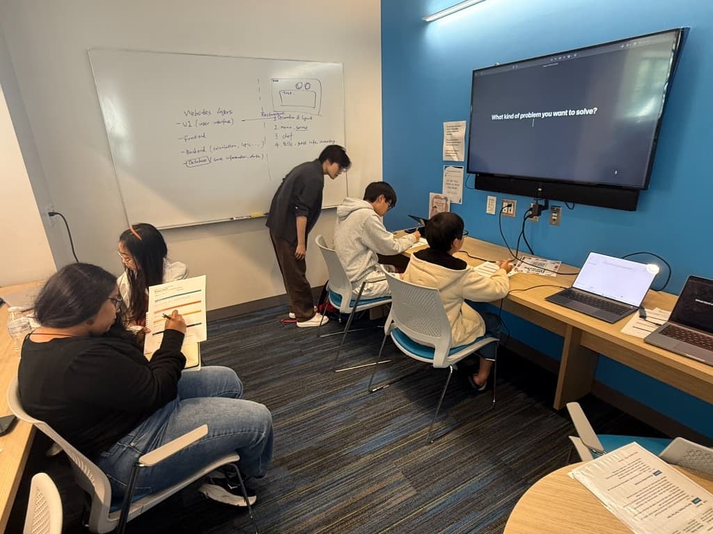 Full classroom view with students working and mentor helping during Vibe Coding
